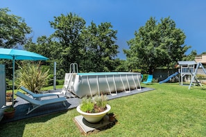 A backyard with a swimming pool, lounge chairs, a small garden, and a slide.