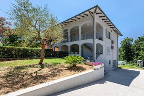 A multi-story building with a balcony, a staircase, and a garden area.