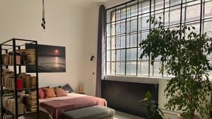 Quarto com cama, estante, janela ampla e planta em vaso.