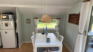 Kompakti keittiö, jossa on mikroaaltouuni ja jääkaappi, ruokapöytä tuoleineen, riippuvalaisin ja ikkunasta avautuva näkymä ulos.
