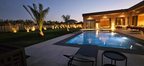 Piscina com espreguiçadeiras, área de estar ao ar livre e uma casa moderna com grandes janelas.