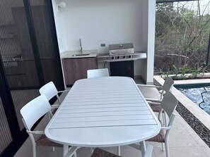 An outdoor dining area with a white table and chairs, a barbecue grill, and a pool. - Tranquil 3-Bedroom home with Pool, Jacuzzi  and BBQ in beautiful Playa Grande (North of the restaurant La Forja)