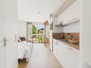 A modern hotel room with a bed, a kitchenette, a dining area, and a view of the outside. - La Houle - studio for 3 people - shared pool (Biscarrosse)