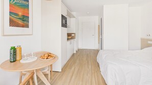 Une chambre d’hôtel avec un lit, une table à manger où le petit-déjeuner est servi, un coin cuisine et un tableau encadré au mur.