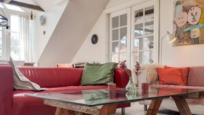 A modern living room with a red leather sofa, a glass coffee table, and a white couch with orange cushions. - 7 Person Holiday Home in Logstrup (Logstrup)