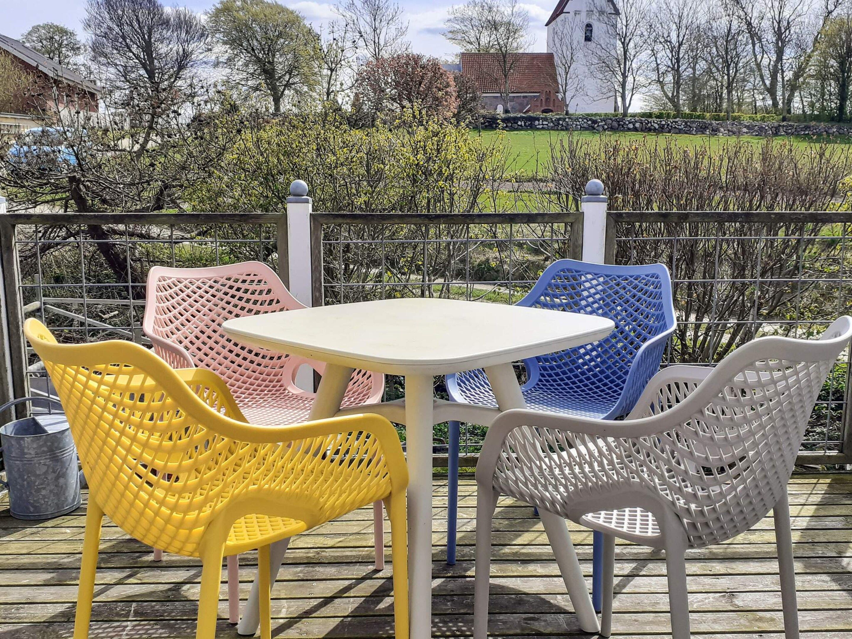 Een terras met een ronde tafel en vier stoelen, een metalen hek en uitzicht op een gebouw en bomen.