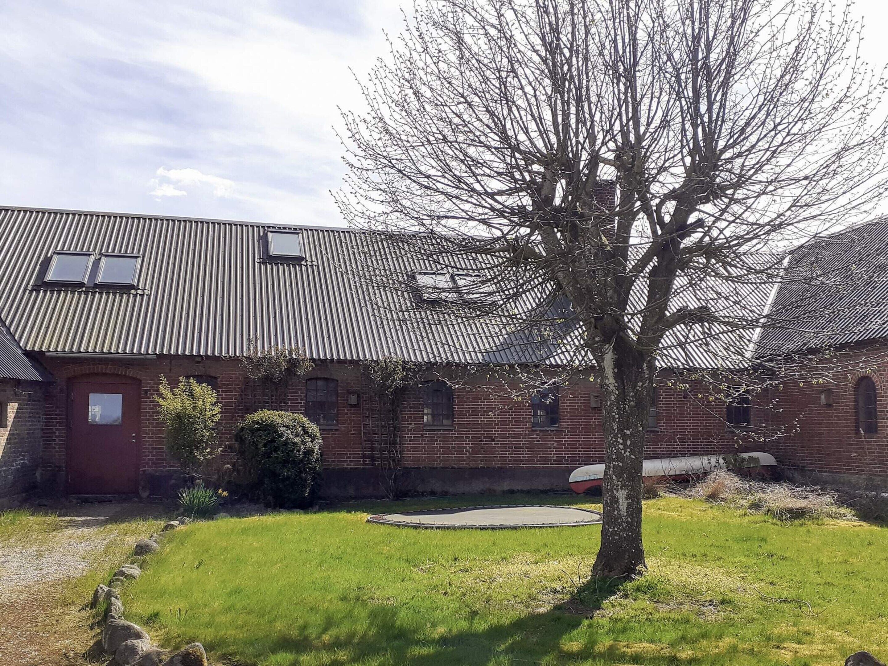 A brick building with a metal roof, a tree in the foreground, and a clear sky.