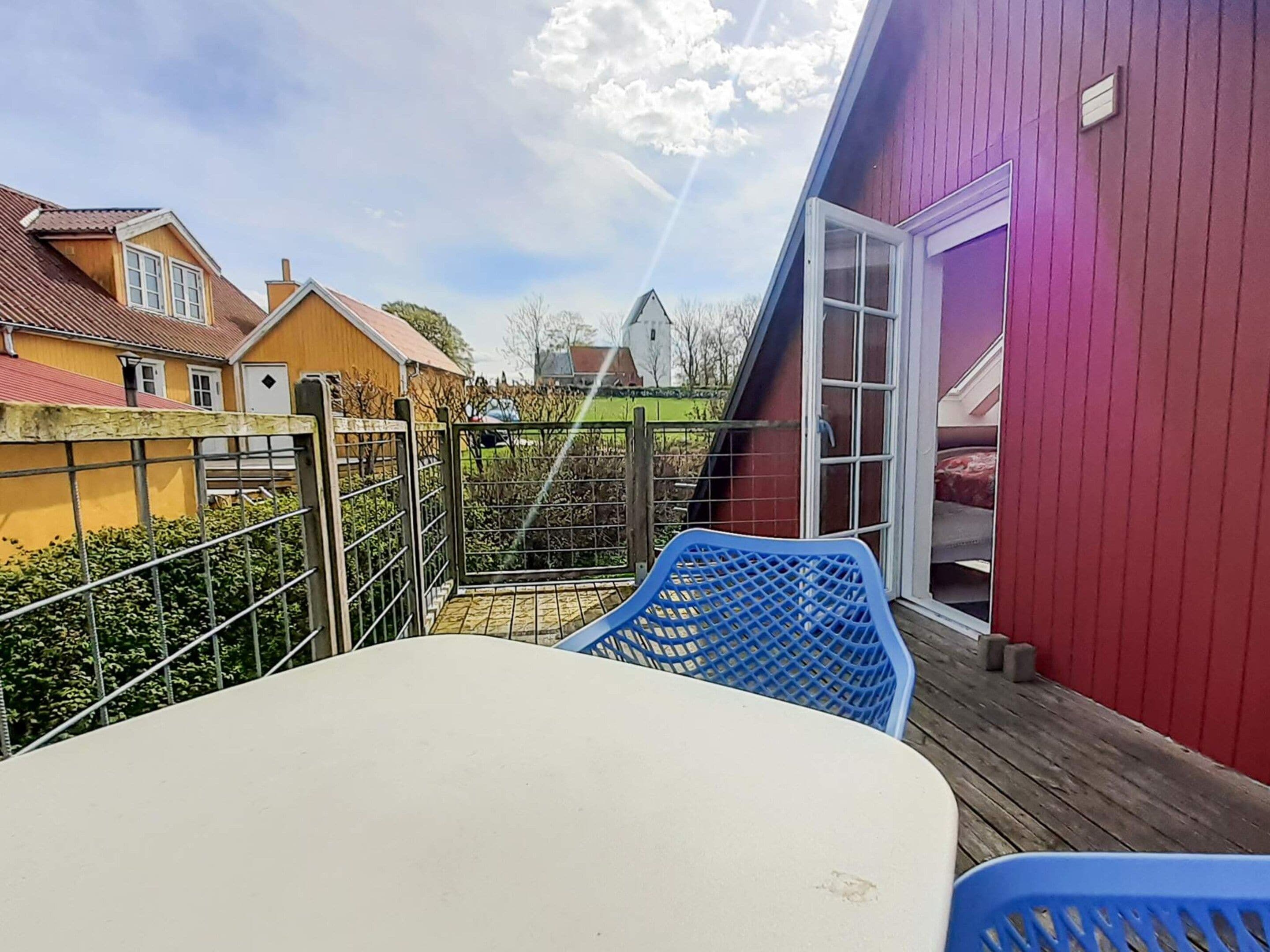 Un balcón con una mesa y sillas, una reja de metal y un edificio rojo al fondo.