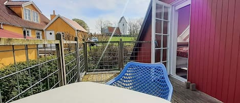 A balcony with a table and chairs, a metal gate, and a red building in the background.