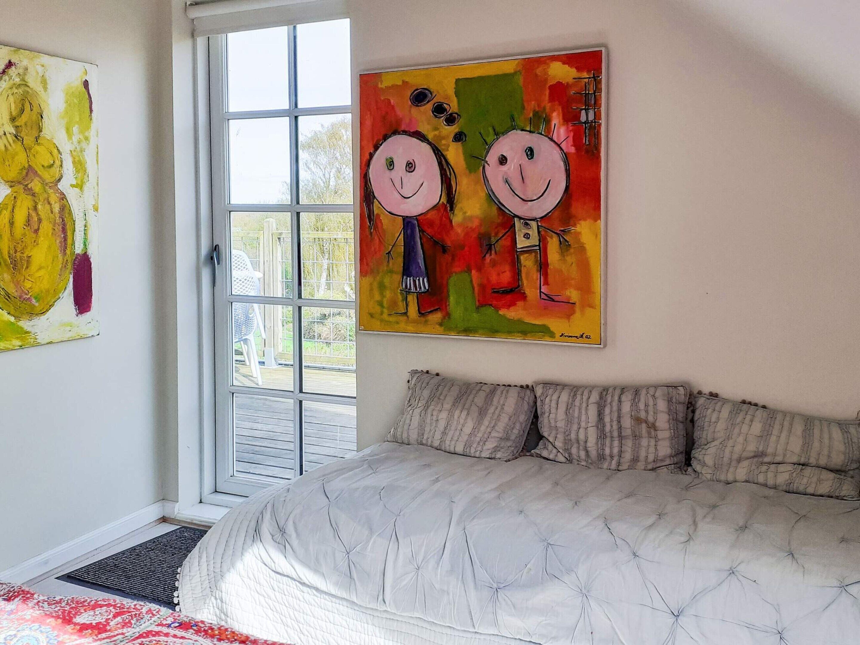 A bedroom with a bed, a window, and two paintings on the wall.