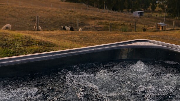 A hot tub with a view of a hilly landscape and sheep grazing.