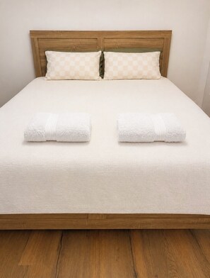 Un letto con una testiera in legno, due cuscini e due asciugamani arrotolati.