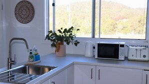 A kitchen with a sink, a microwave, a toaster, and a window with a view of trees.