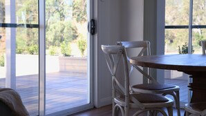 A room with a sliding glass door leading to an outdoor deck, a round wooden table, and two white chairs with woven seats.