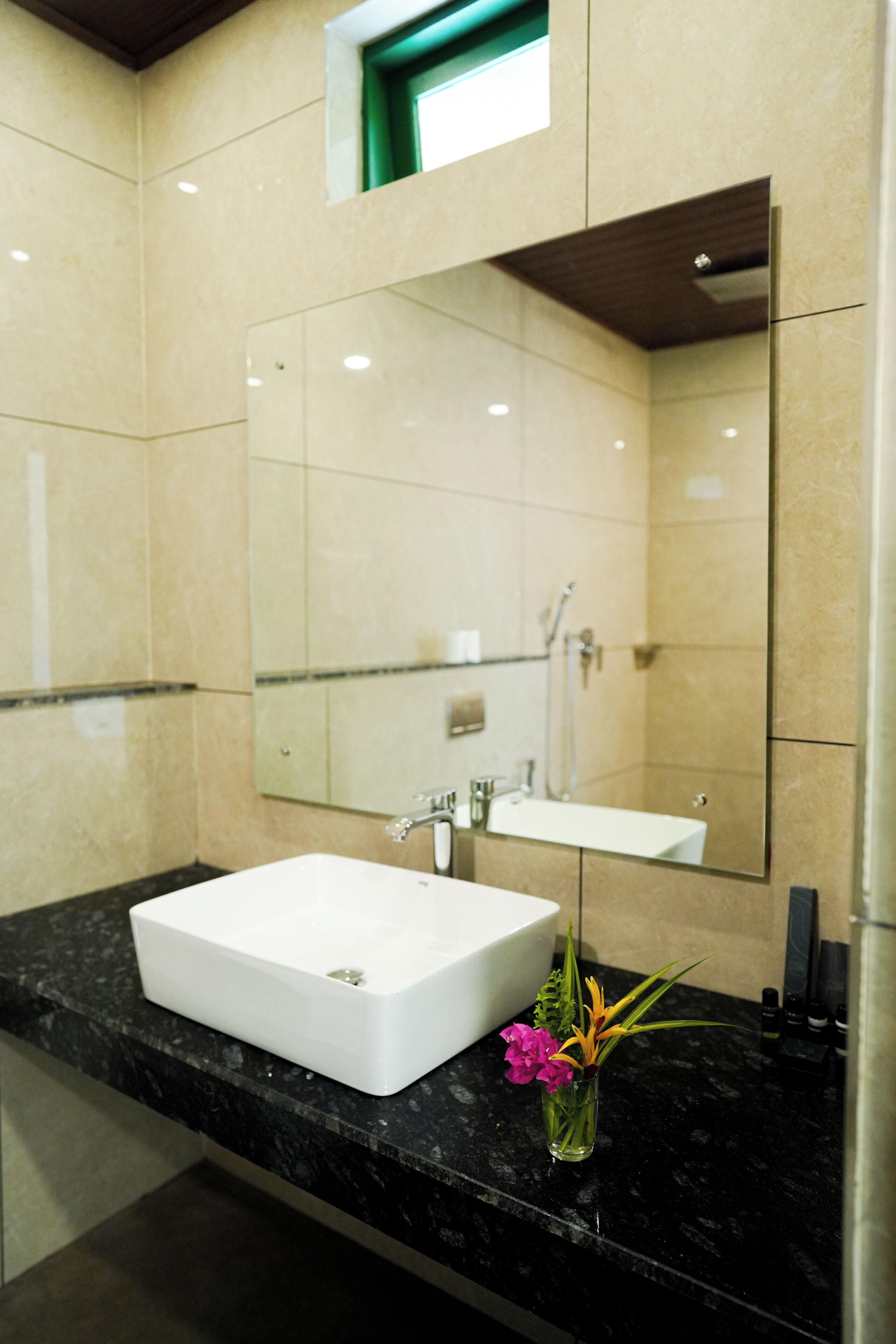 Un baño con un lavabo blanco, un espejo y un florero con flores en la encimera.