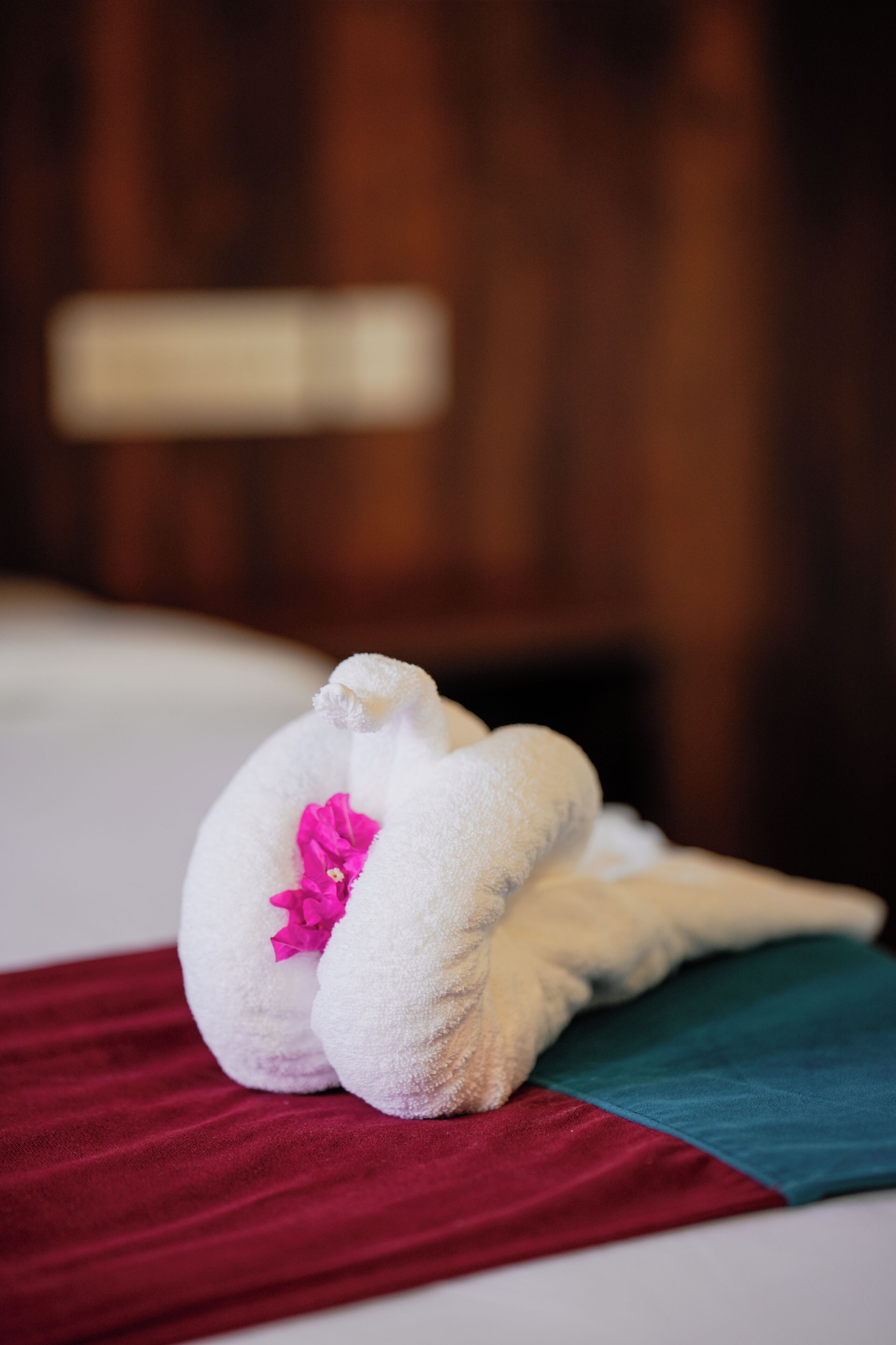 A bed with a white blanket and a red and teal pillow.