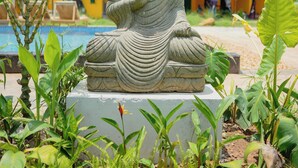 Una estatua de Buda en un jardín, con un edificio amarillo al fondo.