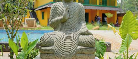 Una estatua de Buda en un jardín, con un edificio amarillo al fondo.