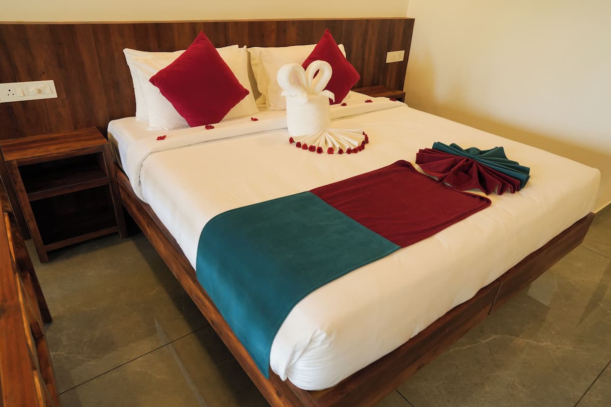Una cama bien hecha con una colcha blanca y verde azulada, almohadas rojas y una decoración central con forma de cisne.