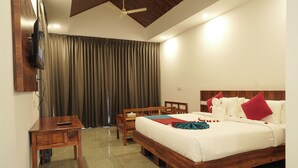 Una habitación de hotel con una cama, un escritorio, una silla, un televisor montado en la pared y un ventilador de techo.