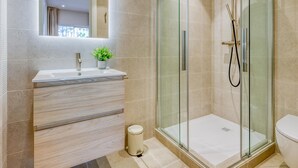 A modern bathroom with a glass-enclosed shower, a vanity with a mirror, and a small potted plant. - Modern apartment near the marina - Estepona (Estepona)