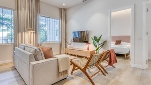 A modern living room with a sofa, a coffee table, a TV, and a bed in the adjacent room. - Modern apartment near the marina - Estepona (Estepona)
