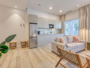 Un saló modern amb un sofà, una taula de dinar, una zona de cuina i un gran finestral amb cortines.