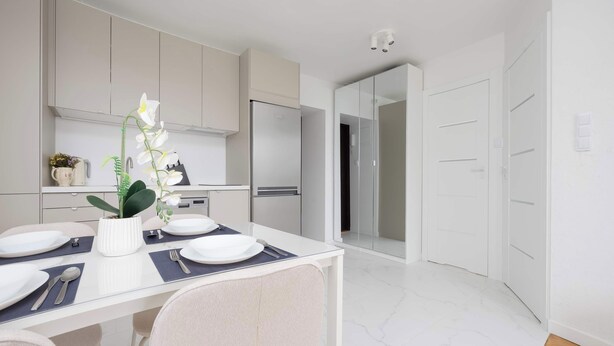 A modern kitchen with white cabinets, a stainless steel refrigerator, and a dining table set for four. - Modern Apartment with a Desk | Air Conditioning | Downtown (Warszawa)