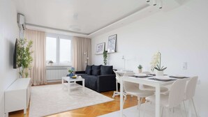 A modern living room with a sofa, dining table, and chairs, a TV, and a window with curtains. - Modern Apartment with a Desk | Air Conditioning | Downtown (Warszawa)