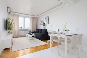 A modern living room with a sofa, dining table, and chairs, a TV, and a window with curtains. - Modern Apartment with a Desk | Air Conditioning | Downtown (Warszawa)