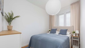 A bedroom with a bed, bedside table, lamp, and a potted plant. - Modern Apartment with a Desk | Air Conditioning | Downtown (Warszawa)