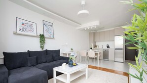 A modern living room with a dark-colored sofa, a white coffee table, and a kitchen in the background. - Modern Apartment with a Desk | Air Conditioning | Downtown (Warszawa)