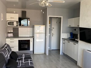 Eine kompakte Küche mit Mikrowelle, Backofen, Kühlschrank und Deckenventilator.
