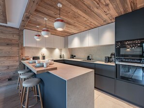 A modern kitchen with a wooden ceiling, bar stools, and a built-in oven. - Ski-in/ski-out apartment - 8 guests (Les Allues)
