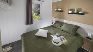 Een moderne slaapkamer met een bed, een raam met gordijnen, een hoofdbord en een plank met decoratieve objecten.