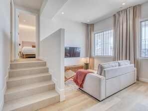 Un salon moderne avec un escalier, un canapé, un téléviseur et une fenêtre avec des rideaux.
