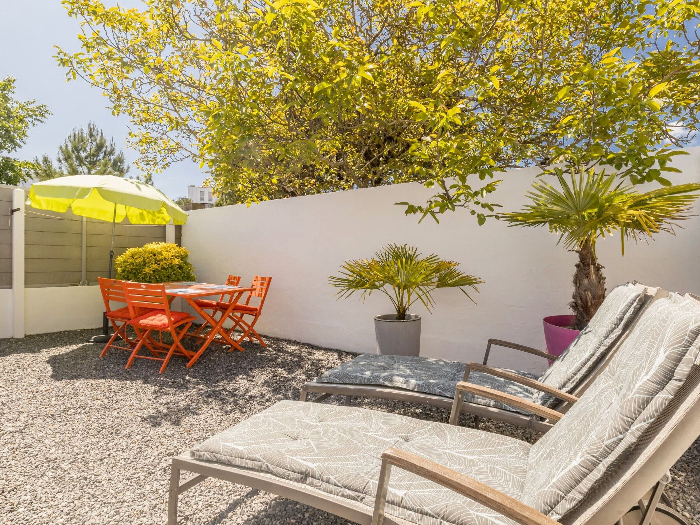 Eine Terrasse im Freien mit Tisch, Stühlen, einem gelben Sonnenschirm, einem Blumentopf und einer Liege.