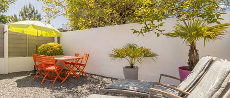 Eine Terrasse im Freien mit Tisch, Stühlen, einem gelben Sonnenschirm, einem Blumentopf und einer Liege.