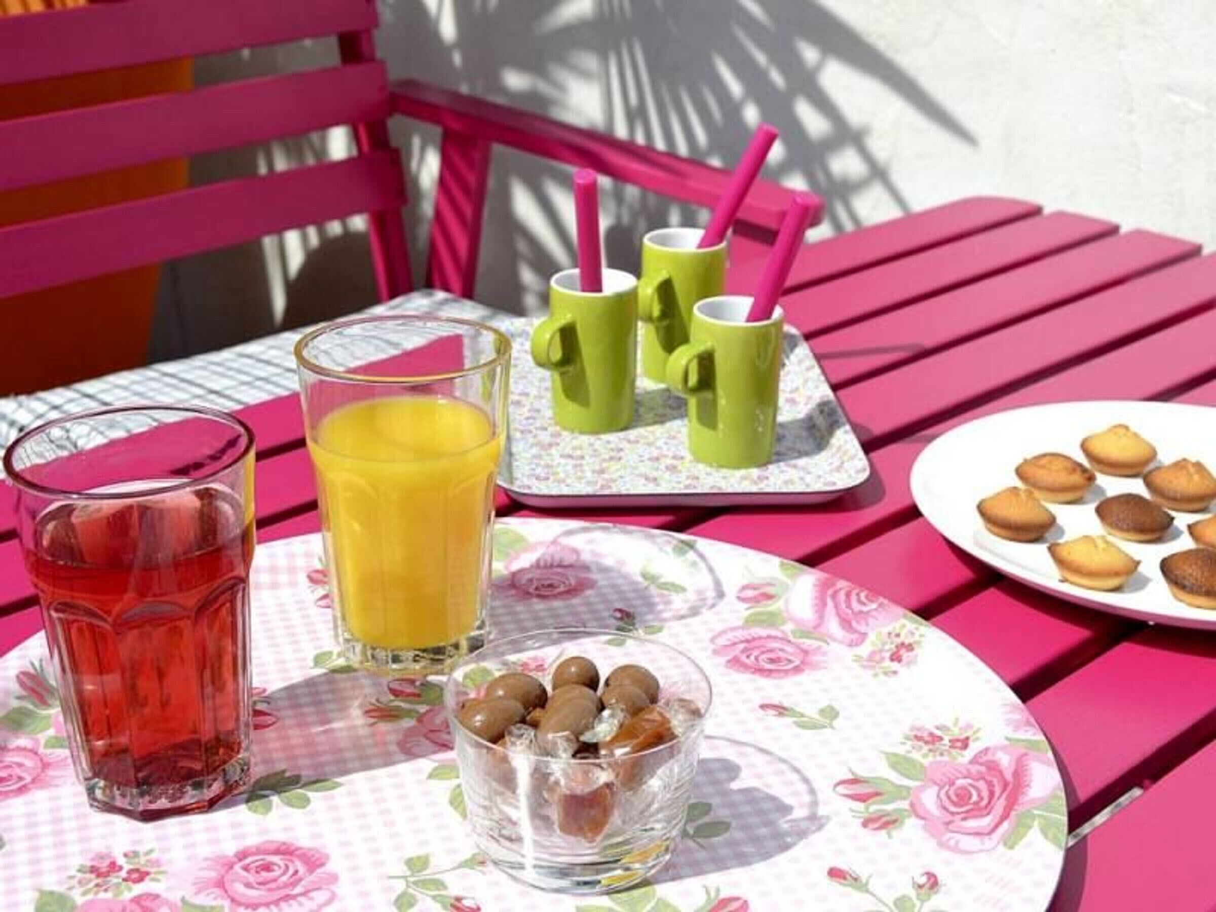 Une table avec un verre de jus d’orange, un verre d’une boisson rouge, une assiette de biscuits et un bol d’olives.