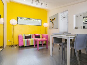 Une pièce lumineuse aux murs jaune vif, avec un canapé à rayures, une petite table et un coin repas.