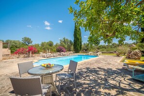 A swimming pool with lounge chairs, a table with a bowl of fruit, and a garden with various plants and flowers. - SON SERRA DE DALT 6 people privat pool wifi Felanitx (Felanitx)