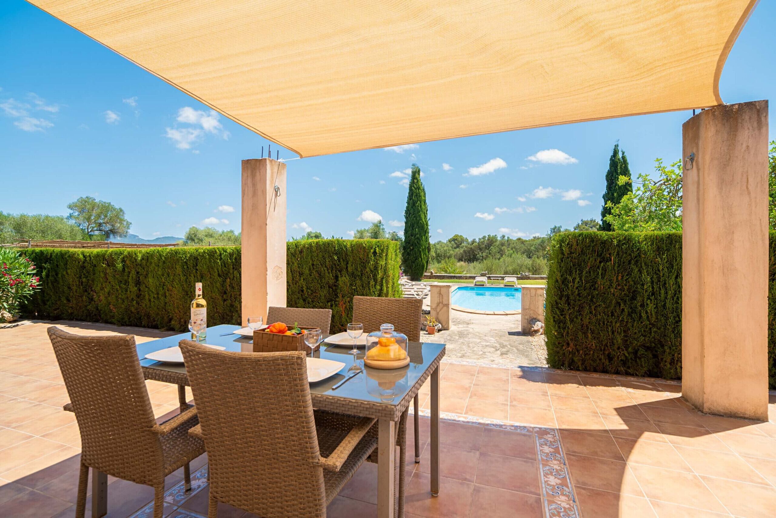Eine Terrasse im Freien mit Esstisch, umgeben von Korbstühlen und Blick auf Pool und Landschaft.