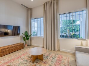 A modern living room with a round wooden coffee table, a sofa, a TV mounted on the wall, and large windows with curtains. - Modern apartment in Estepona marina (Estepona)