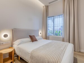 A modern bedroom with a large bed, a bedside table, and a window with curtains. - Modern apartment in Estepona marina (Estepona)