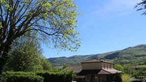 A rural house with a tiled roof, surrounded by greenery and hills.
