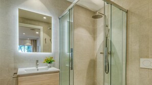 Un baño moderno con ducha envuelta en vidrio, tocador de madera, lavabo blanco y retrete.