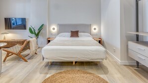Un dormitorio moderno con cama, mesitas de noche, televisor, planta y una silla de mimbre.