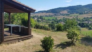 A wooden structure with a table, surrounded by a rural landscape with fields and hills. - Mobile home with air conditioning - 6 guests (Saint-Point)