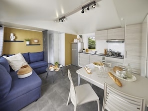 A modern kitchen with a dining area, a sofa, and a small table with food and drinks. - Mobile home with air conditioning - 6 guests (Saint-Point)
