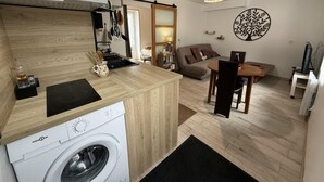 A compact kitchen with a washing machine, a dining area with a table and chairs, and a living area with a sofa and a decorative wall piece. - Peaceful cottage, parking, pets allowed (Saint-Georges-sur-Cher)